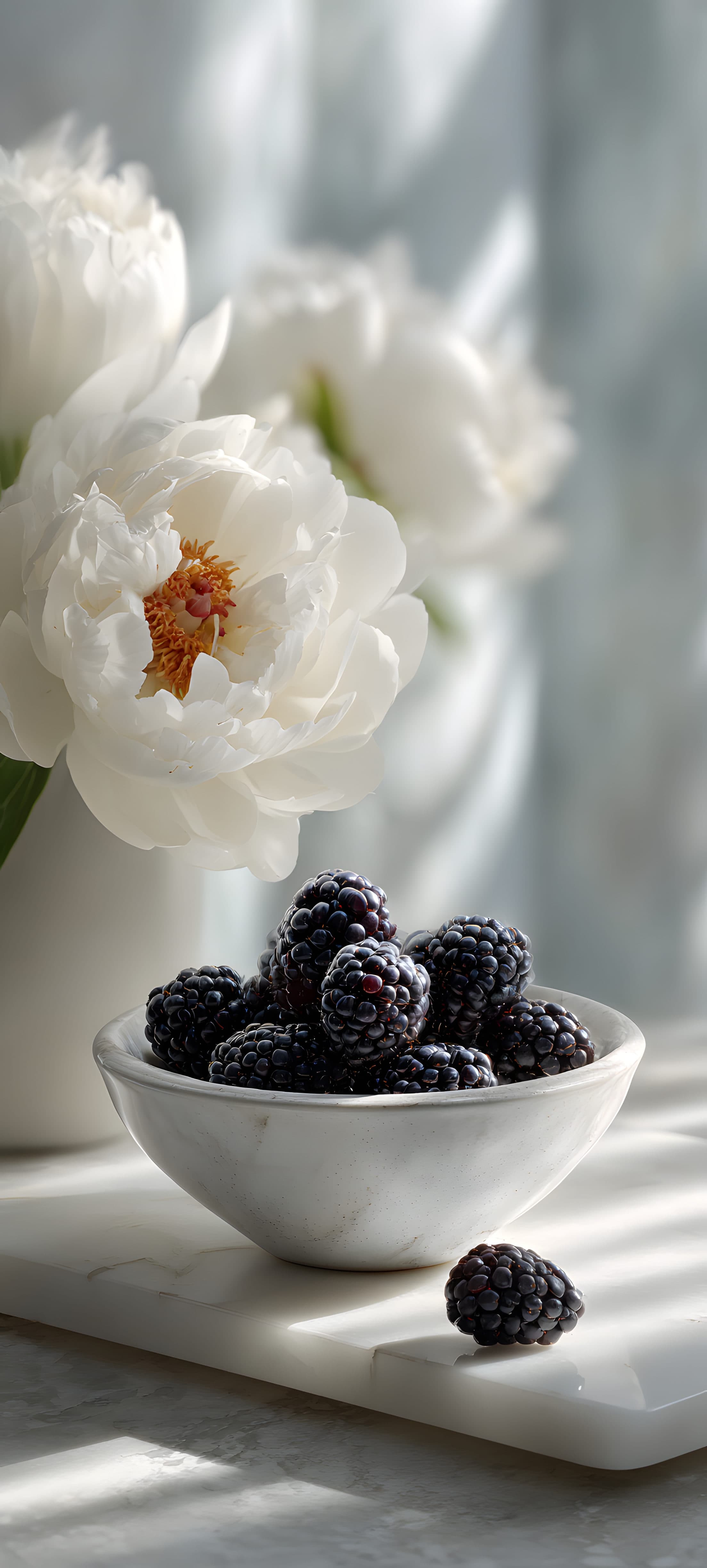 White flowers and blueberries in a bowl on a marble surface, with soft natural lighting.